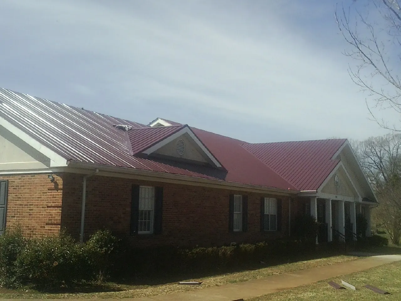 Red metal roof with gabled entries on a long brick building, from a Hail Damage Roof Repair job in Rixeyville