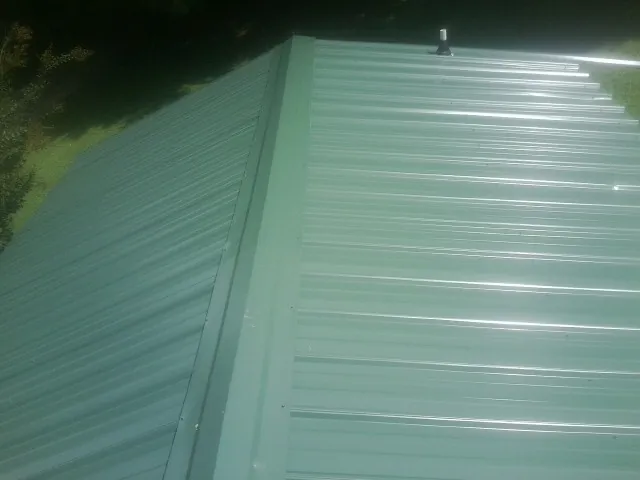 New green metal panels meeting at the ridge of a roof — Flat Roof Repair work by our crew in Rixeyville