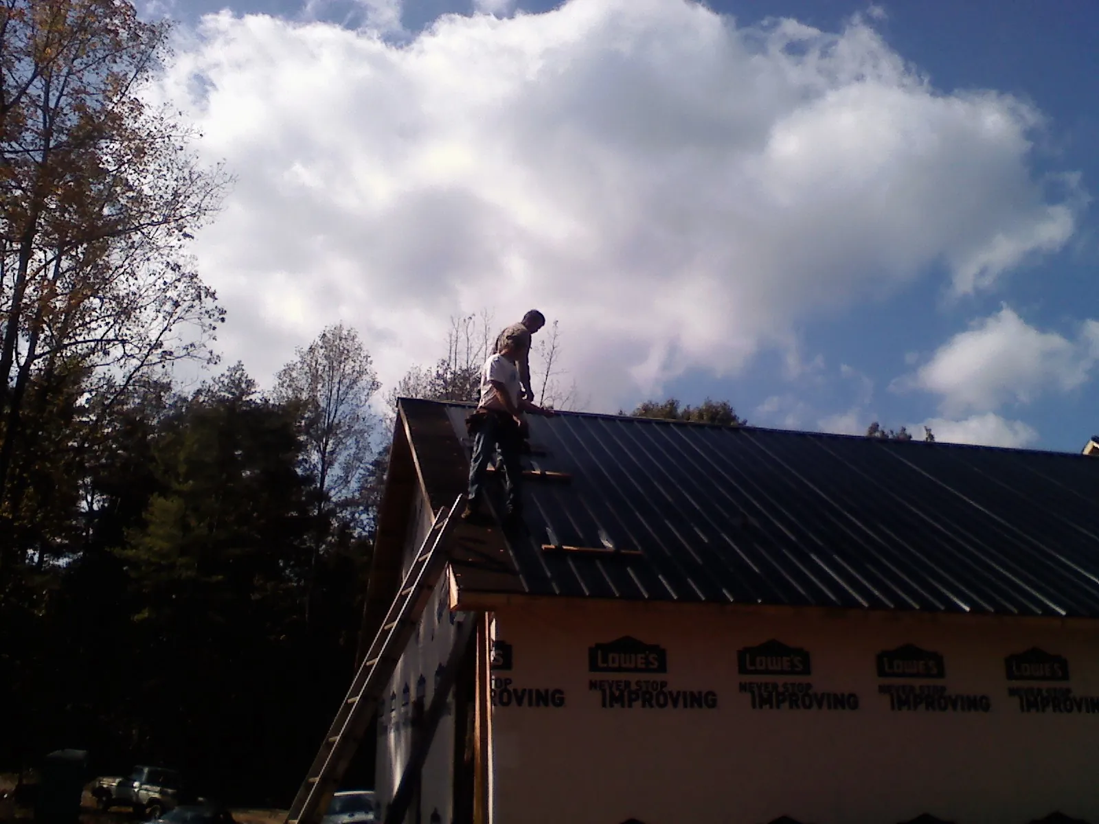 Roofer fastening dark metal panels high against a cloudy sky, from a Roof Inspection job in Rixeyville