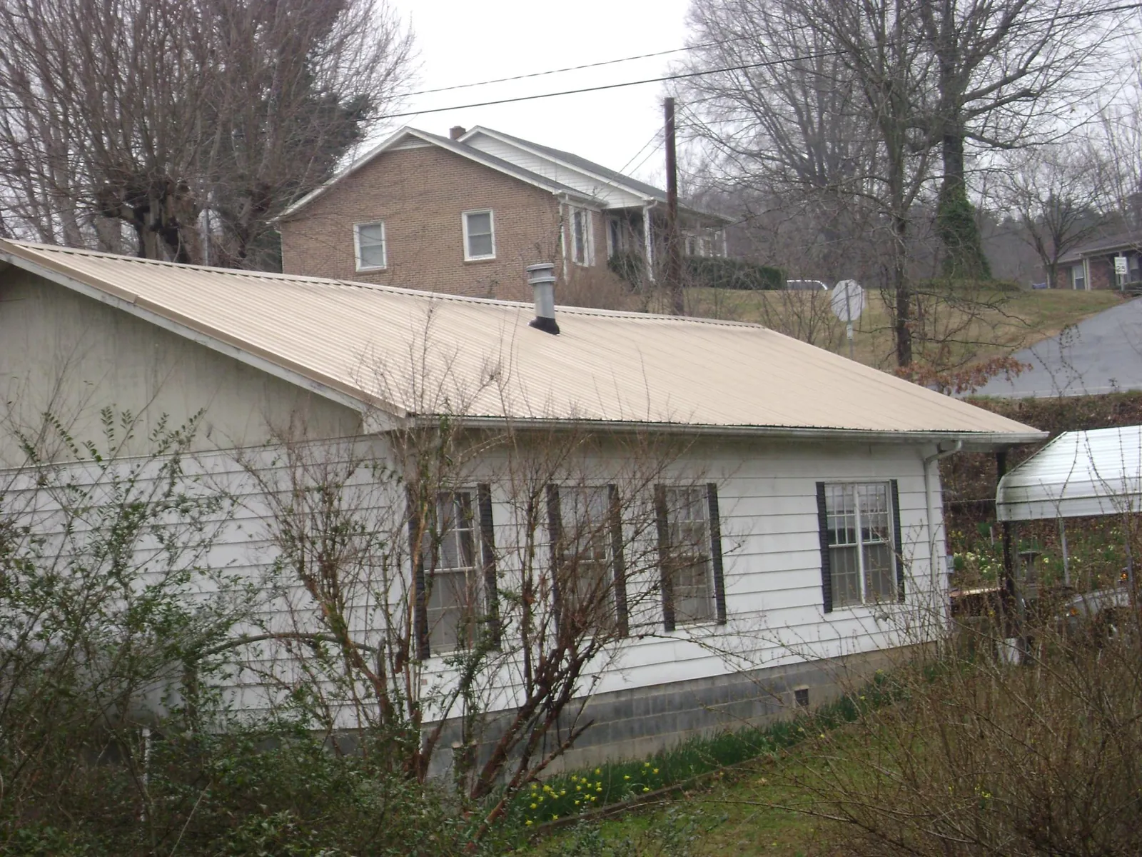 Tan metal roof on a white sided house set into a hillside — Commercial Roofing by Roofing Brothers in Rixeyville